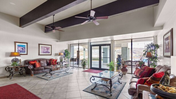 A spacious living room with a high ceiling, ceiling fans, a large window, and a view of the outdoors.