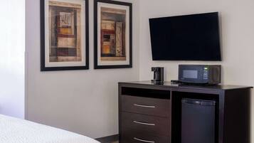 A hotel room with a bed, a dark wooden dresser with a microwave and a small refrigerator, and two framed abstract paintings on the wall.