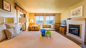A hotel room with a large bed, a fireplace, a television, and a view of the mountains through the windows.
