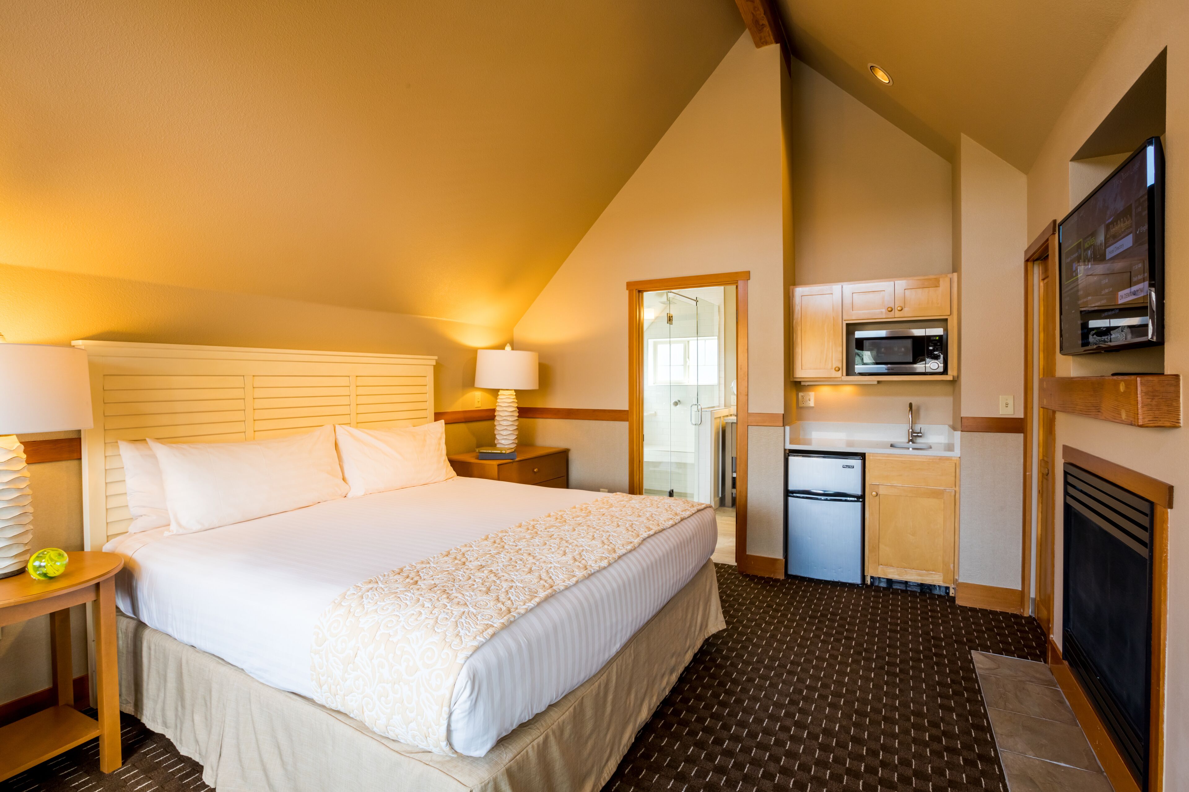 A hotel room with a large bed, a desk, a lamp, a microwave, a refrigerator, and a TV.