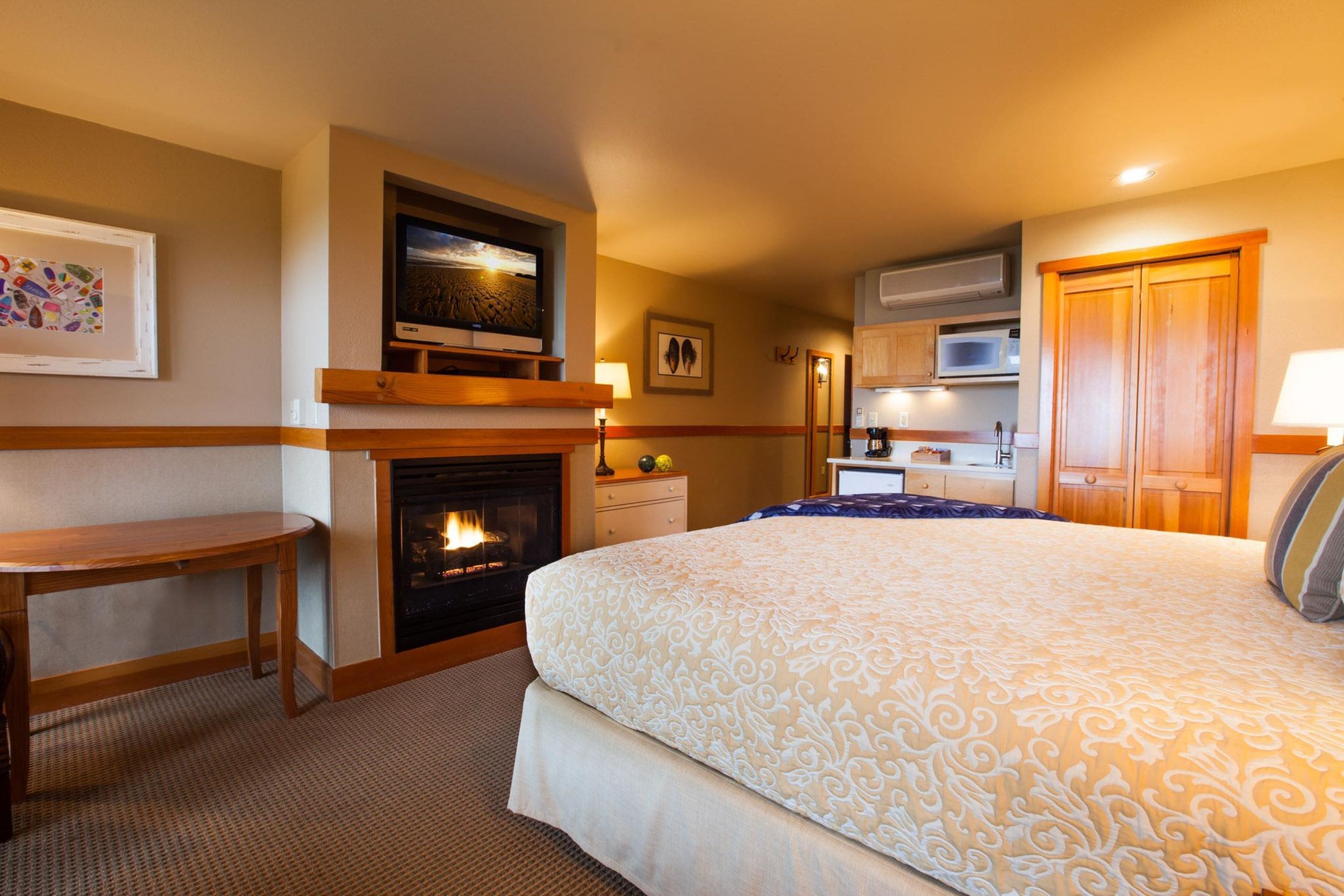 A hotel room with a bed, a desk, a fireplace, a television, and a kitchenette.