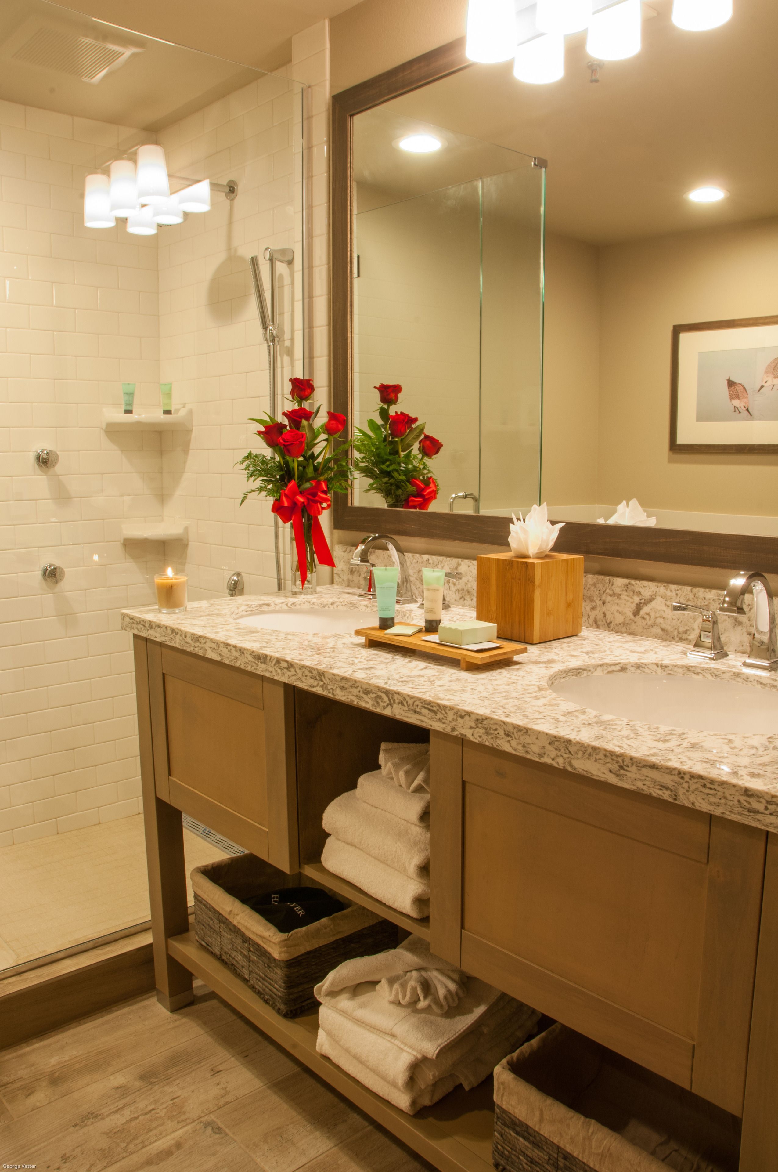 A bathroom with a marble sink, a glass shower enclosure, and a mirror with a framed picture.