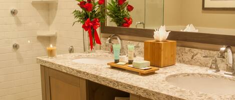 A bathroom with a marble sink, a glass shower enclosure, and a mirror with a framed picture.