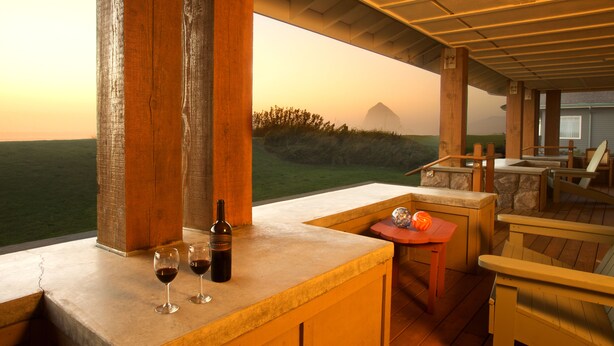 A wooden deck with a view of the landscape, a bar area with a bottle and glasses, and outdoor seating. - The Ocean Lodge (Cannon Beach)