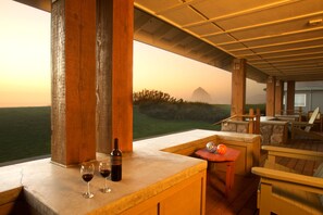 A wooden deck with a view of the landscape, a bar area with a bottle and glasses, and outdoor seating. - The Ocean Lodge (Cannon Beach)