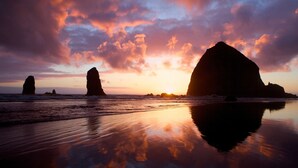 A beach with large rock formations and a sunset. - The Ocean Lodge (Cannon Beach)