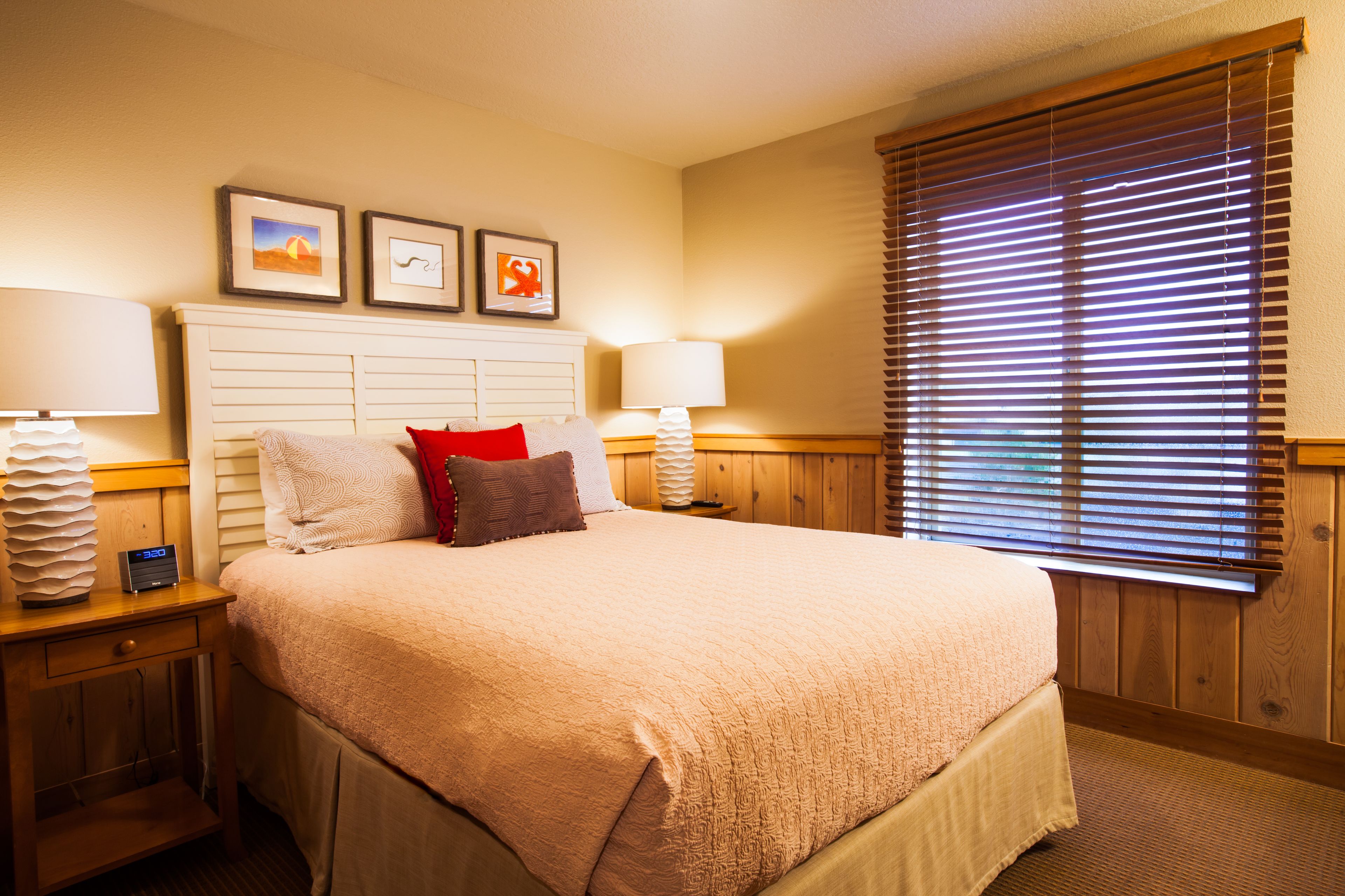 A neatly made bed with a beige comforter, two bedside lamps, and a wooden headboard.