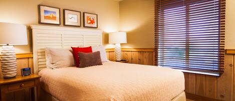 A neatly made bed with a beige comforter, two bedside lamps, and a wooden headboard.
