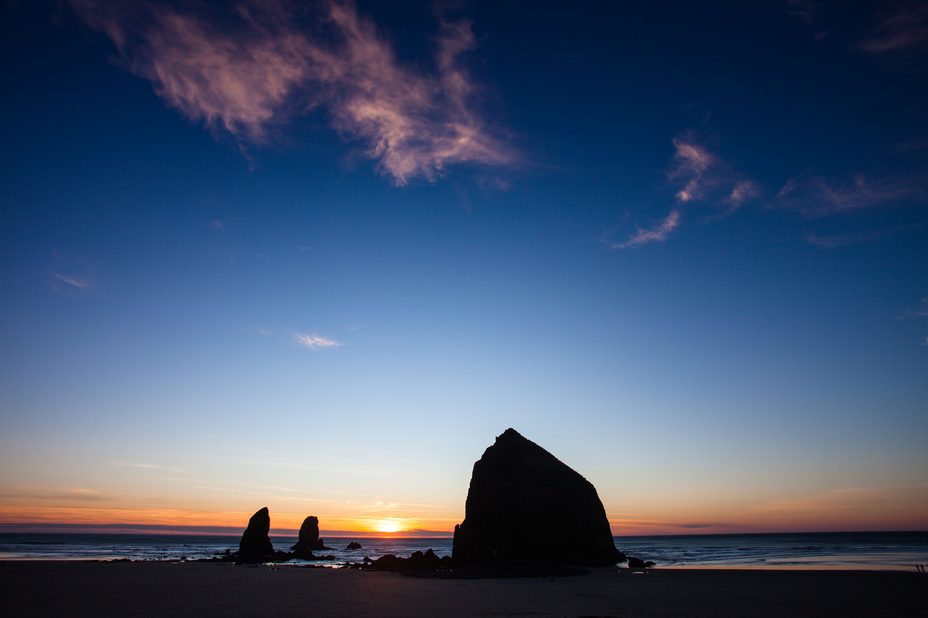 A beach with large rock formations silhouetted against a sunset sky.