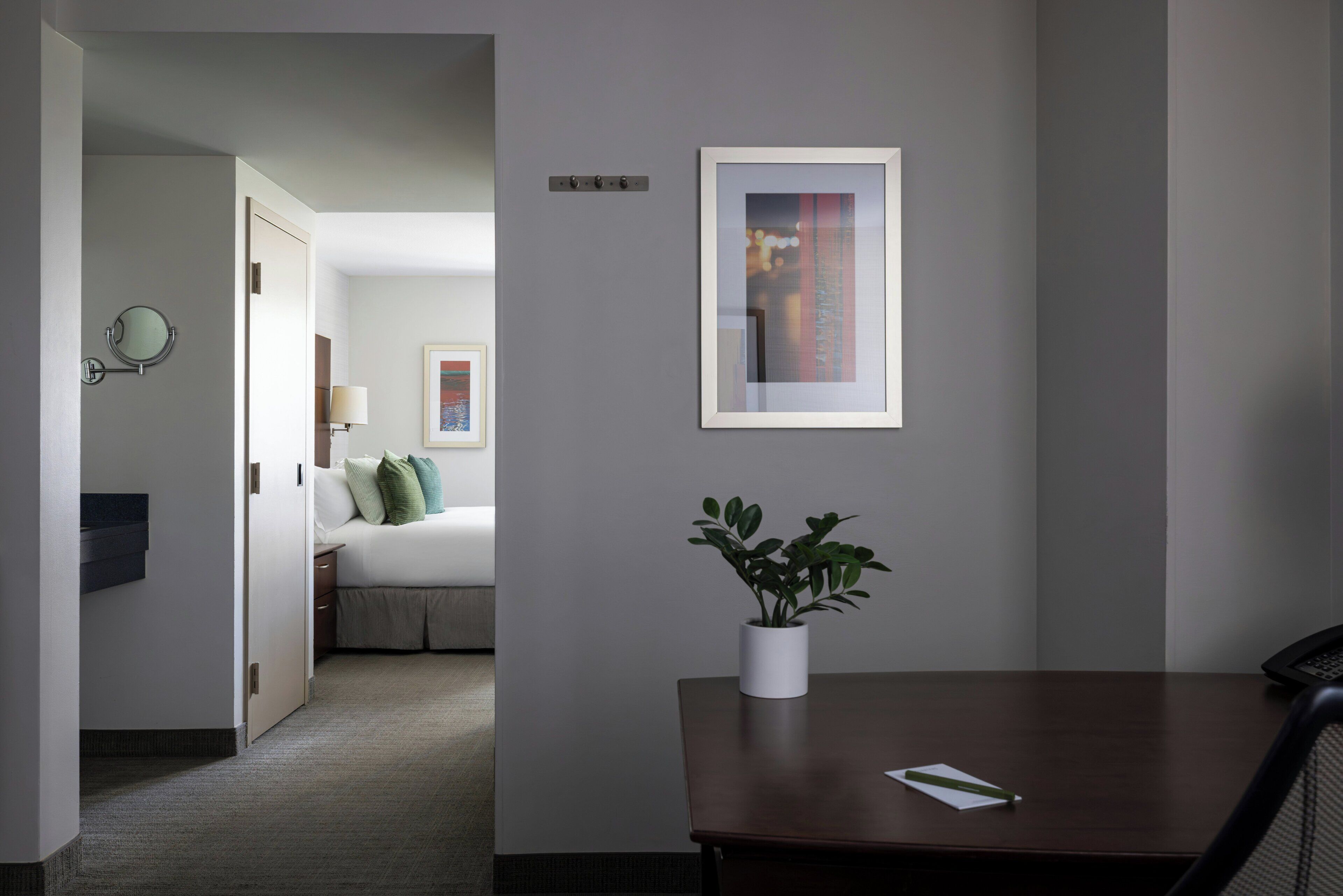 Een hotelkamer met een bed, nachtkastje, een bloempot, een ingelijst kunstwerk aan de muur en een bureau met stoel.
