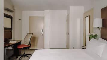 Ein Hotelzimmer mit einem Bett, einem Schreibtisch mit Stuhl, einem kleinen Tisch mit Lampe und einer Tür.