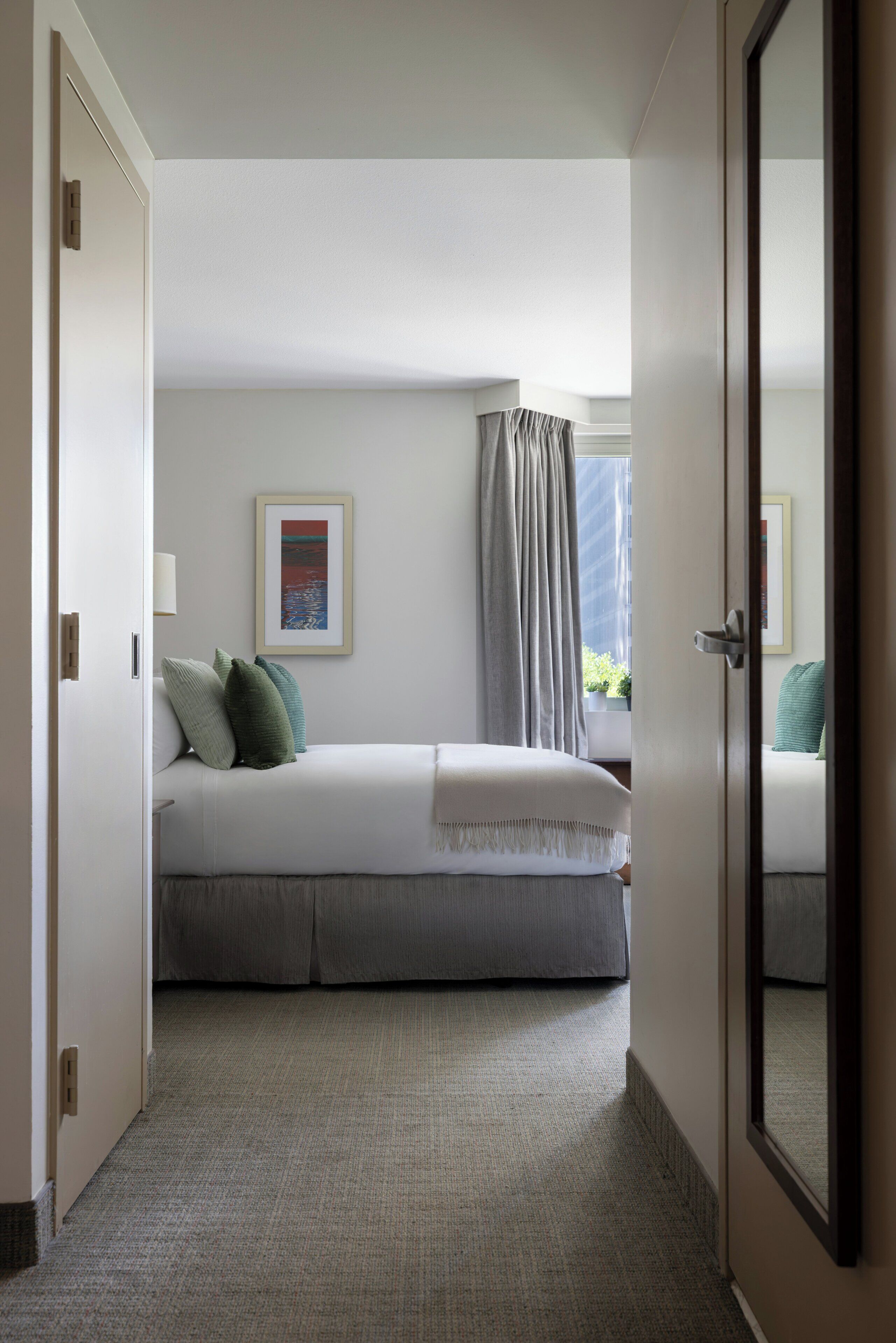 A hotel room with a bed, a framed picture on the wall, and a window with curtains.