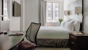 A hotel room with a bed, a desk, a chair, a TV, a window with curtains, and a nightstand with lamps. - Club Quarters Hotel Embarcadero, San Francisco (San Francisco)