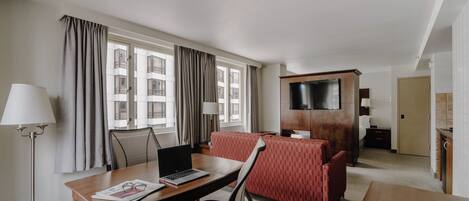 A hotel room with a desk, chair, laptop, and a red sofa.