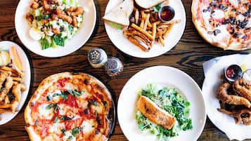 Variedad de platillos, como pizza, ensalada y sándwiches, sobre una mesa de madera.