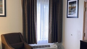 A room with a single chair, a window with curtains, a wall-mounted air conditioner, and a framed picture. - Red Lion Inn & Suites Post Falls (Post Falls)
