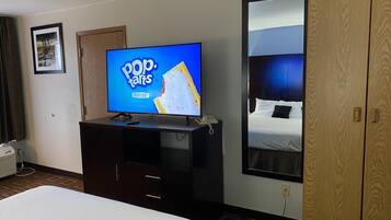 A hotel room with a bed, a TV displaying 'Pop. Tarts' advertisement, a wooden wardrobe, and a large mirror reflecting the bed.