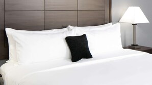 A neatly made bed with white linens and a single black pillow, a bedside lamp, and a wooden headboard. - Red Lion Inn & Suites Post Falls (Post Falls)