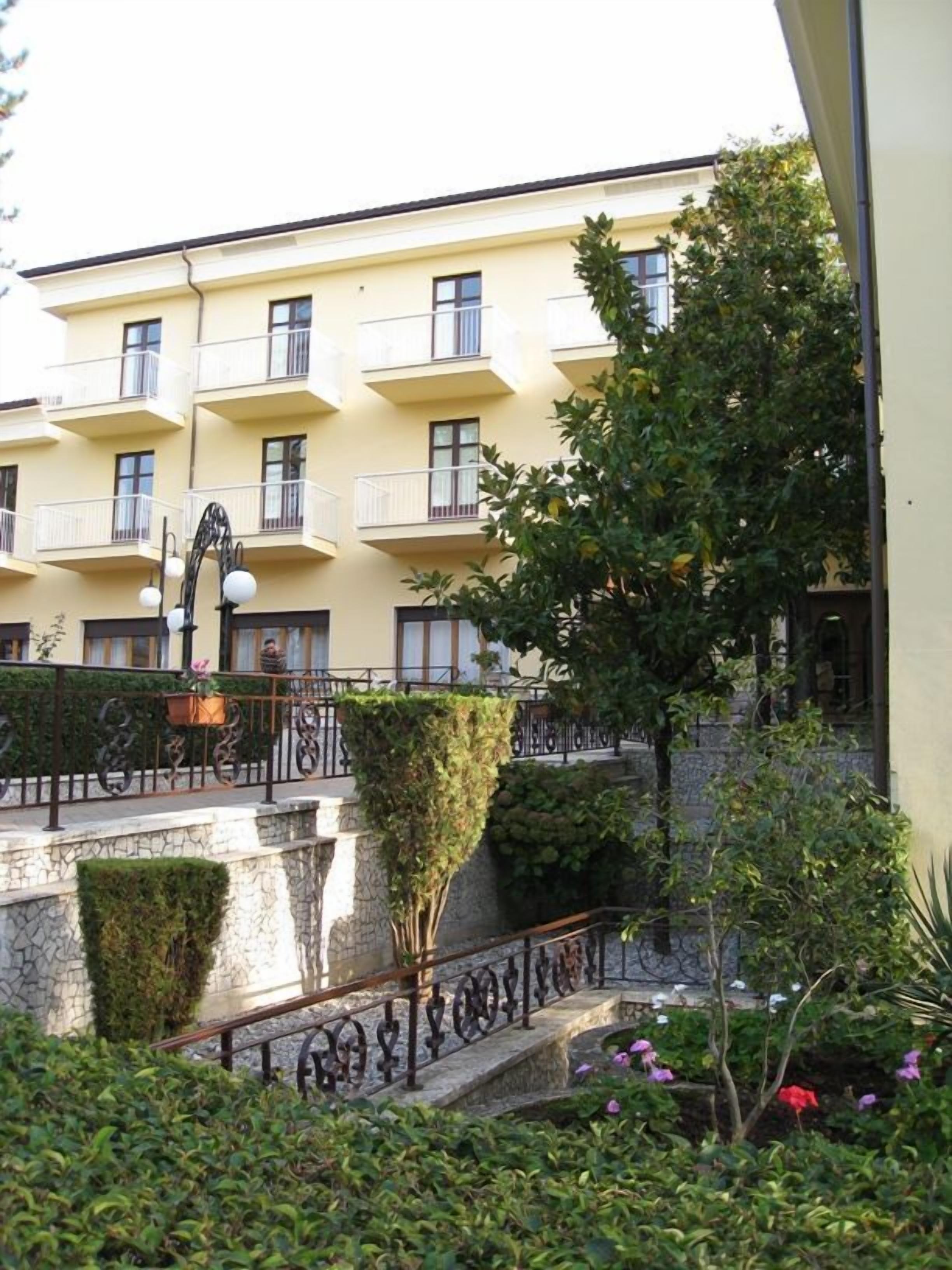 Un edificio a più piani con balconi, una scala in pietra e vegetazione circostante.