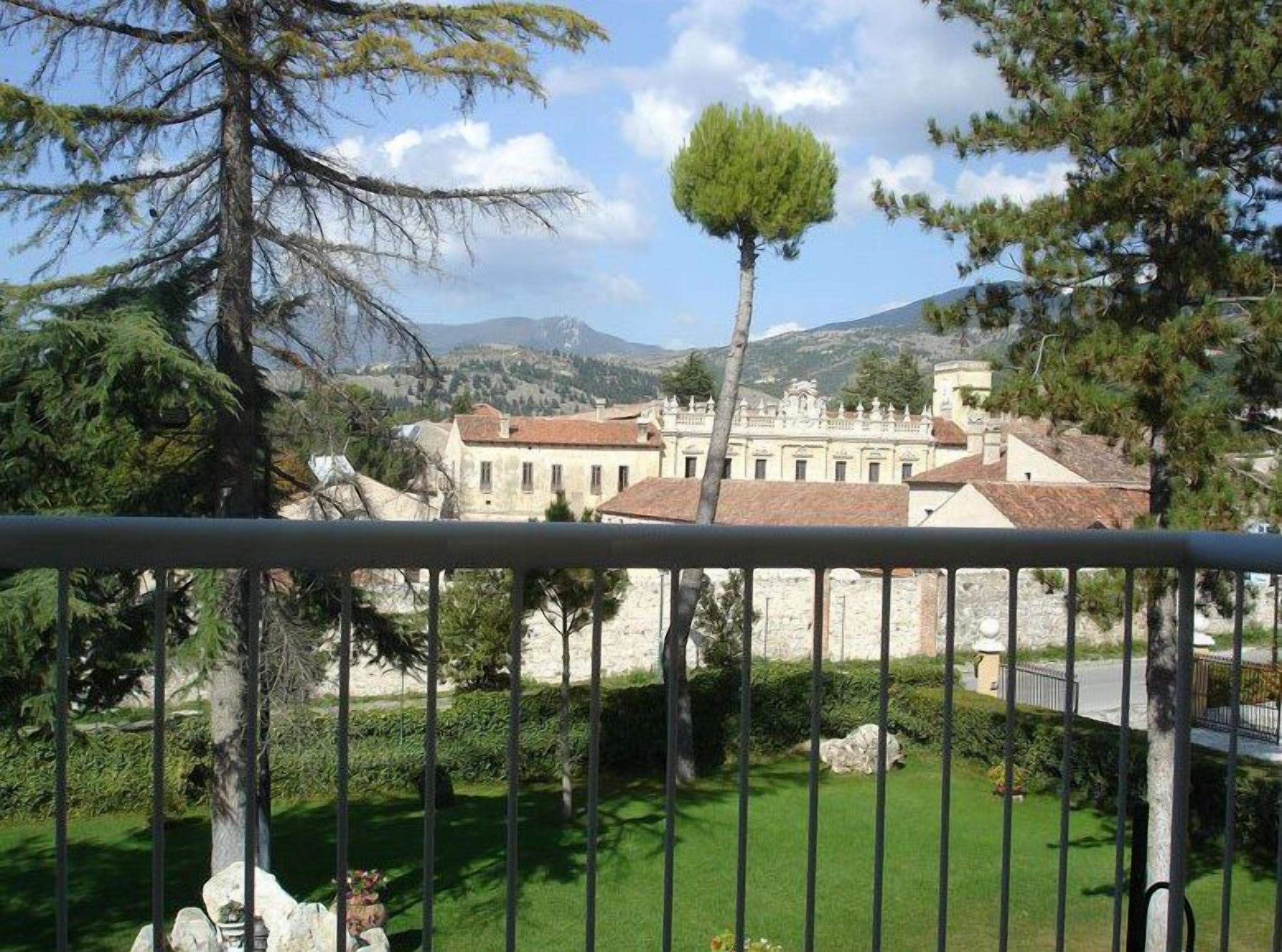 Una vista di un complesso di edifici storici con architettura in pietra, circondato da vegetazione e montagne sullo sfondo.