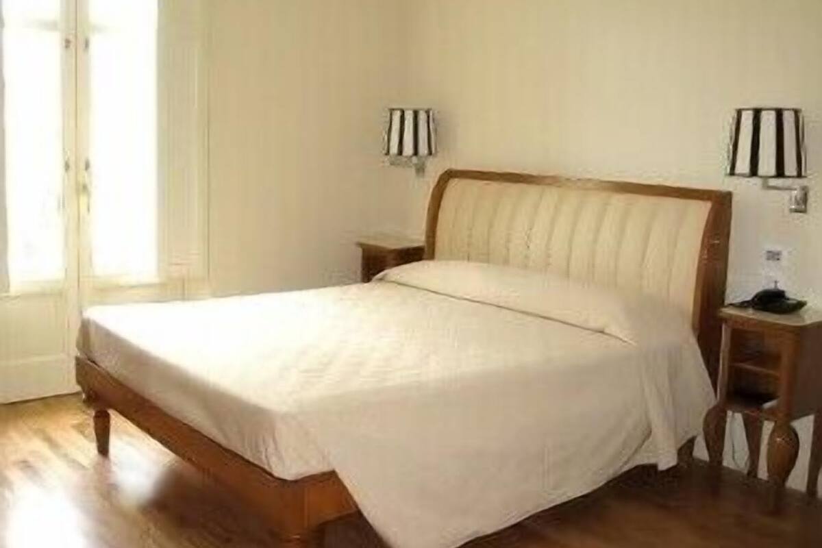 A bedroom with a wooden bed, two bedside tables, and two wall-mounted lamps.