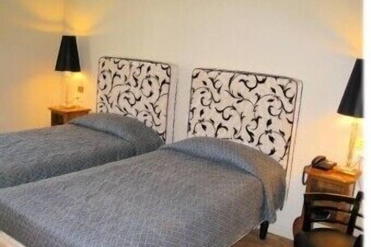 A room with two single beds, each with a patterned headboard, a bedside table, and a lamp.