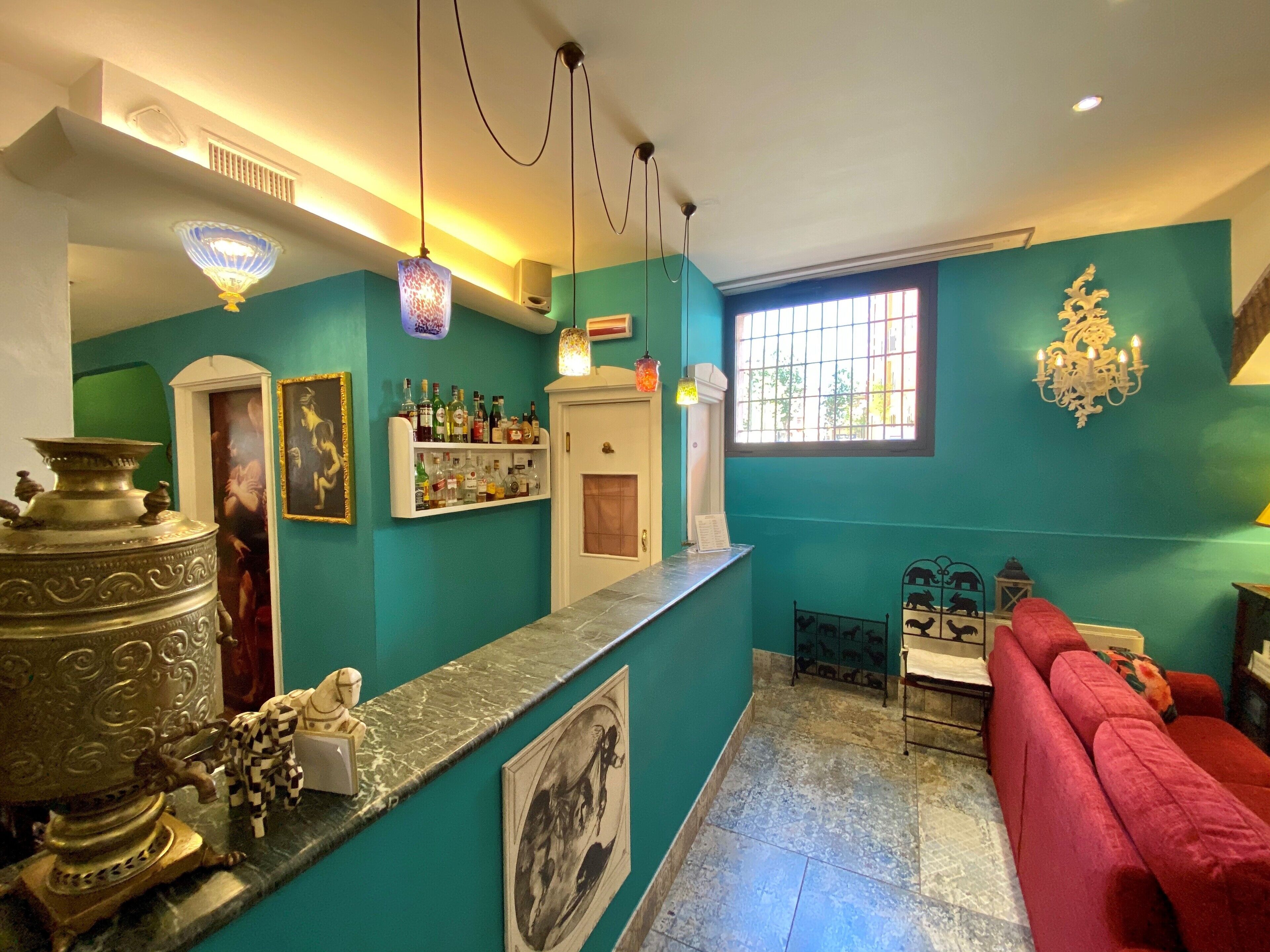 A room with teal walls, a red sofa, a marble counter, and a variety of decorative items including a chandelier, a large metal sculpture, and framed pictures.