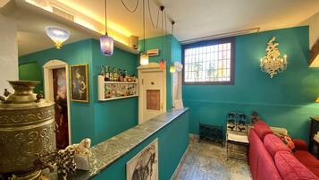 A room with teal walls, a red sofa, a marble counter, and a variety of decorative items including a chandelier, a large metal sculpture, and framed pictures.
