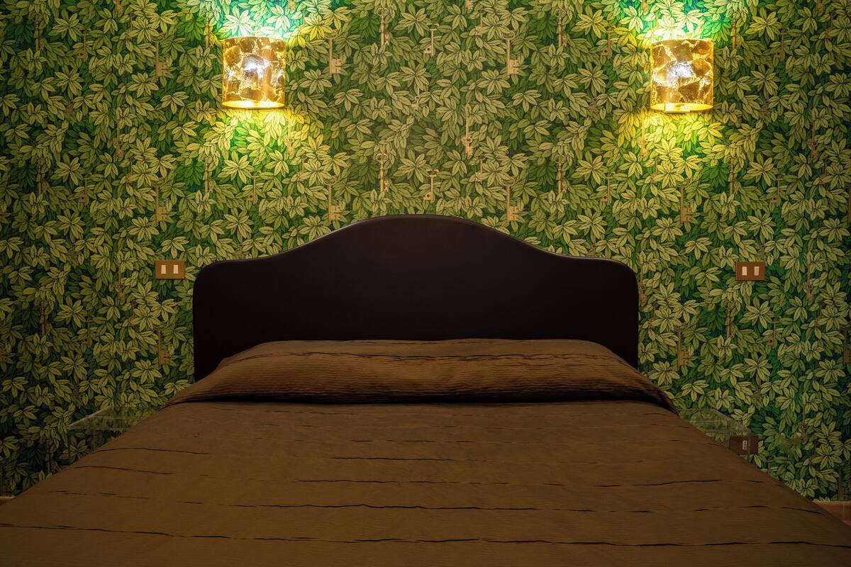 A bed in a room with a green leafy wallpaper and two wall-mounted lights.