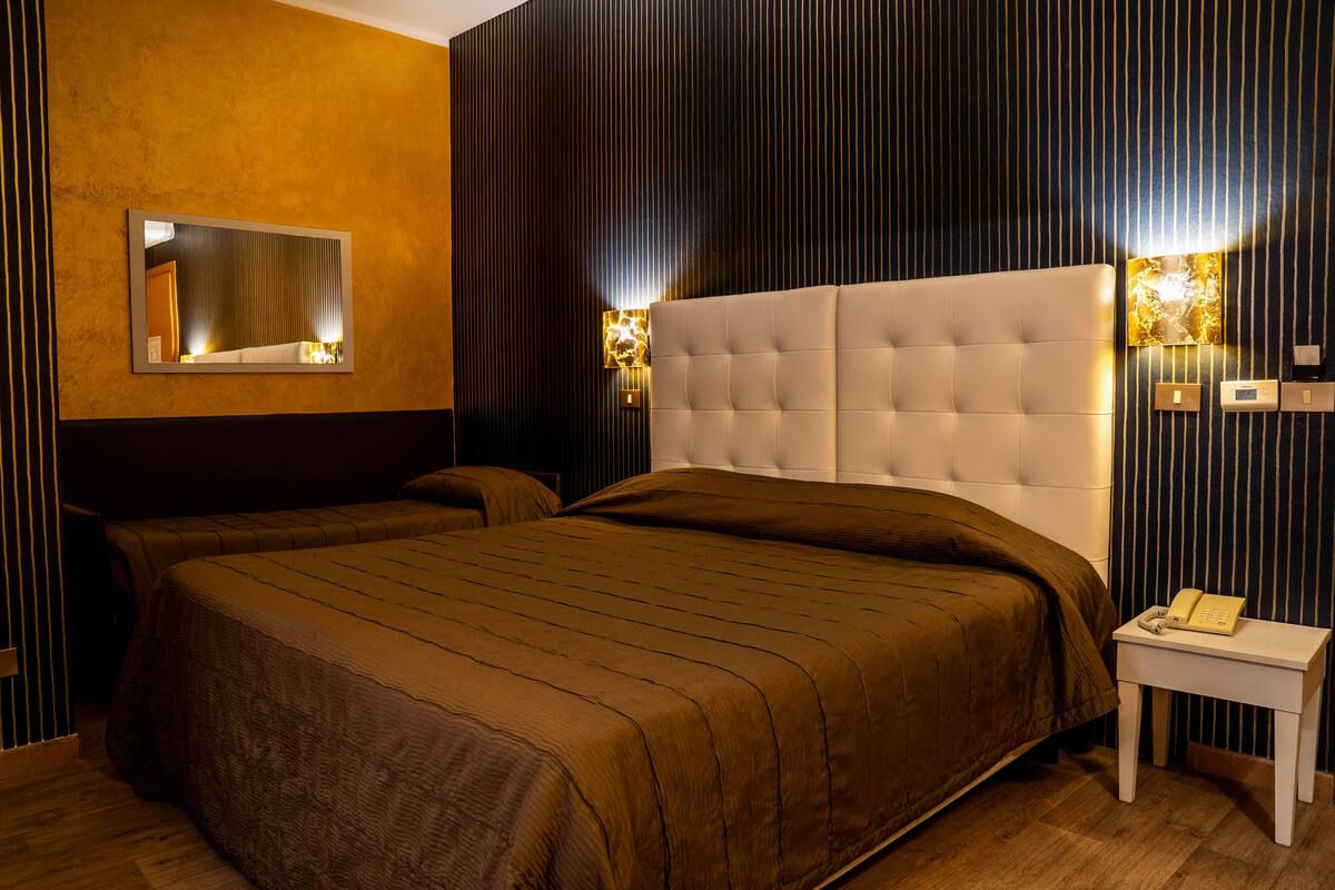 A hotel room with a large bed, a bedside table with a telephone, and two wall-mounted lamps.