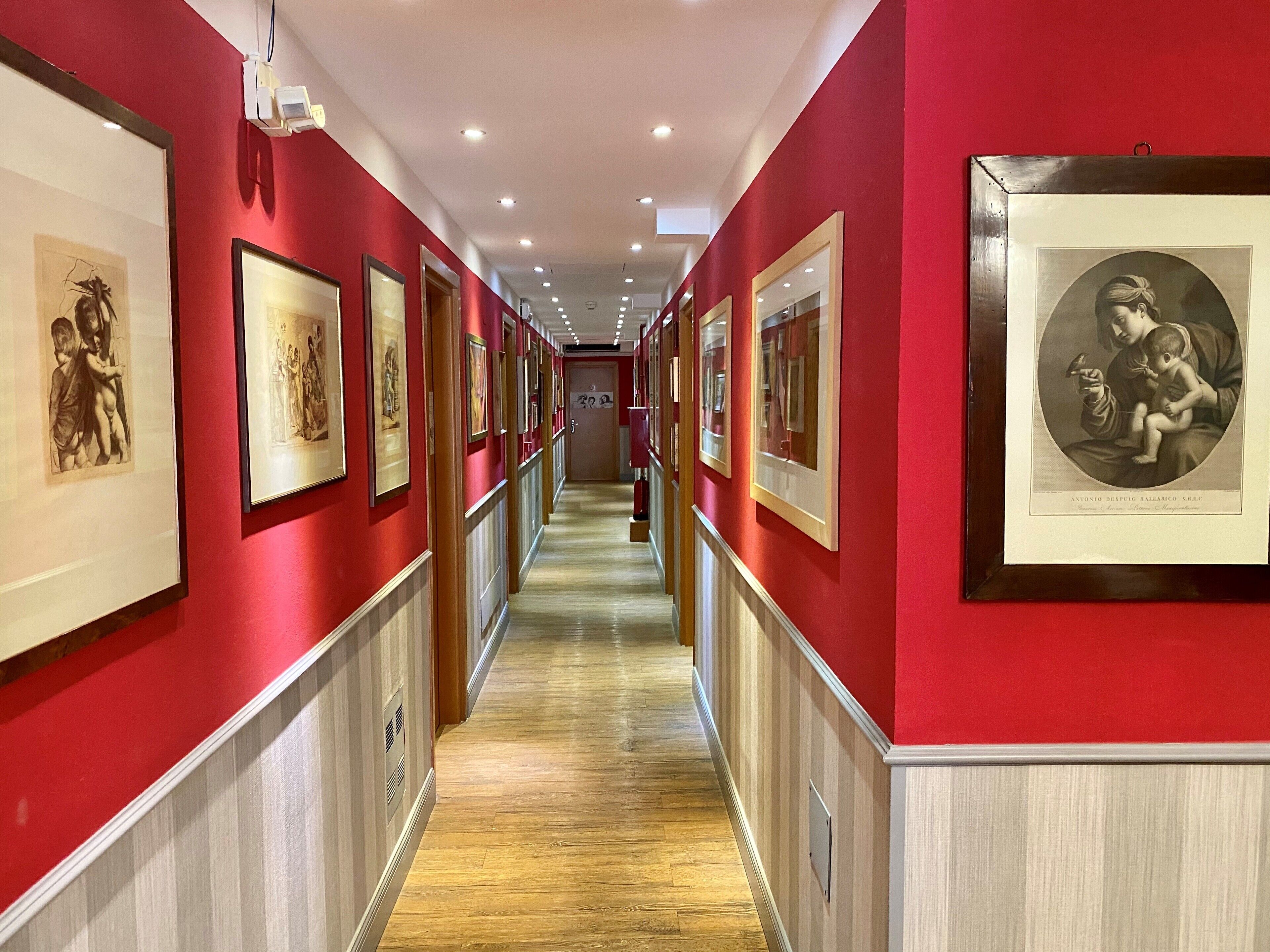 Un corridoio con pareti rosse, opere d'arte incorniciate su entrambi i lati e pavimento in legno.
