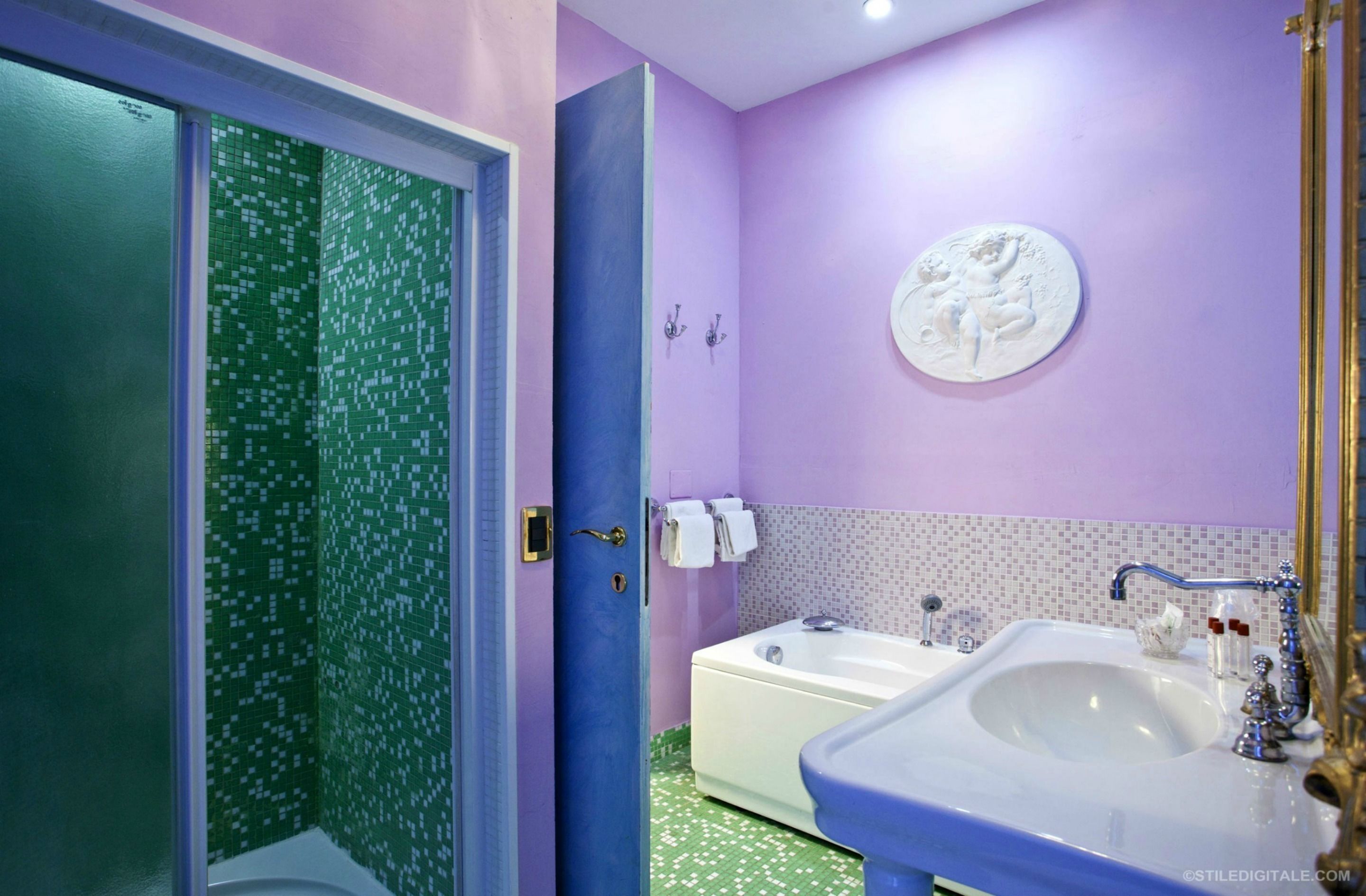 Un bagno con doccia verde, vasca da bagno bianca e lavandino con rubinetto dorato.