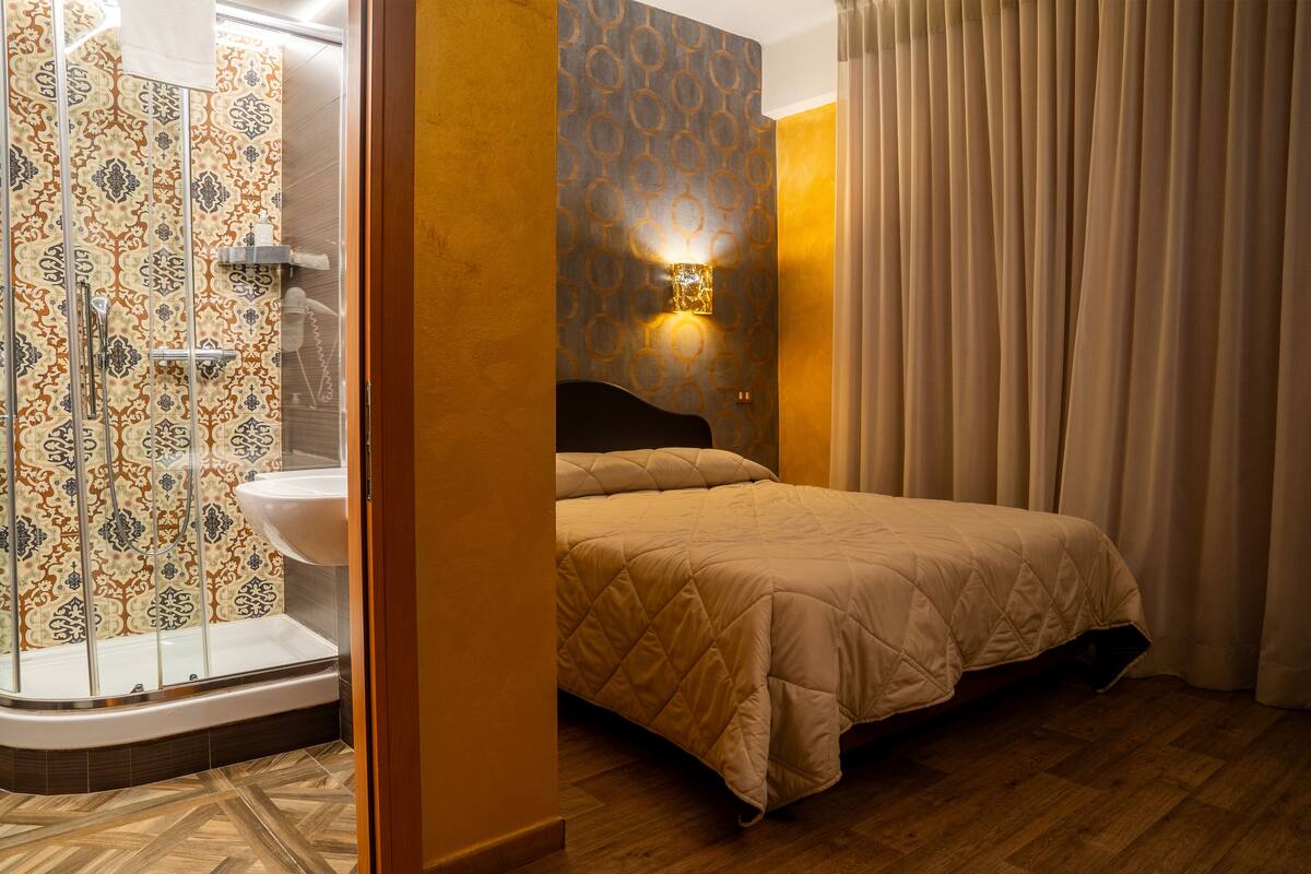 A hotel room with a shower, a bed, and a wall-mounted light fixture.