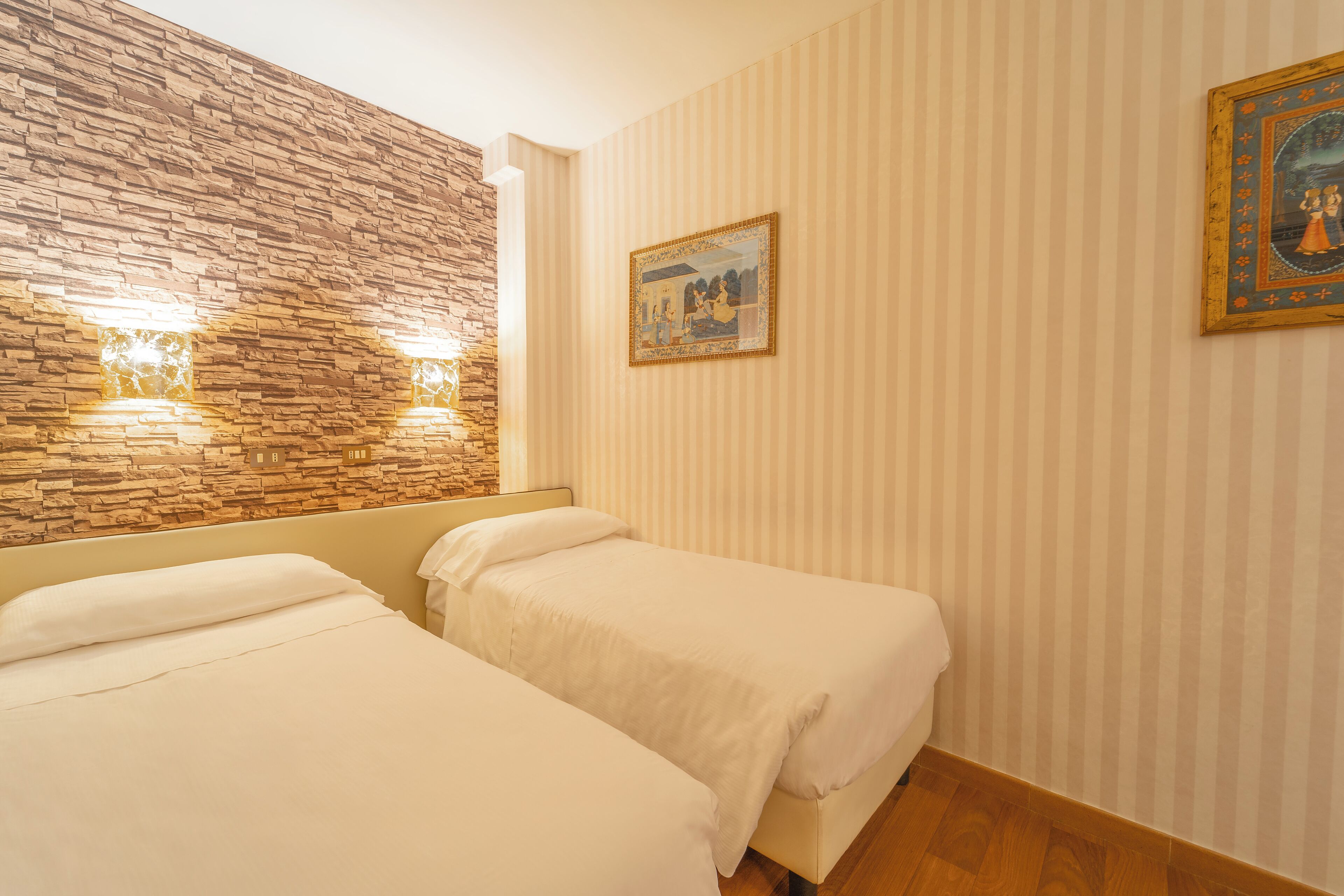 A hotel room with two beds, a stone accent wall, and a painting on the wall.
