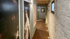 A hallway with a brick wall, wooden floor, and a door with a poster. - Hotel Il Guercino (Bologna)