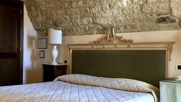 Un dormitorio con techo de piedra, una cama con colcha acolchada, una mesita de noche con lámpara y un aparador con espejo.