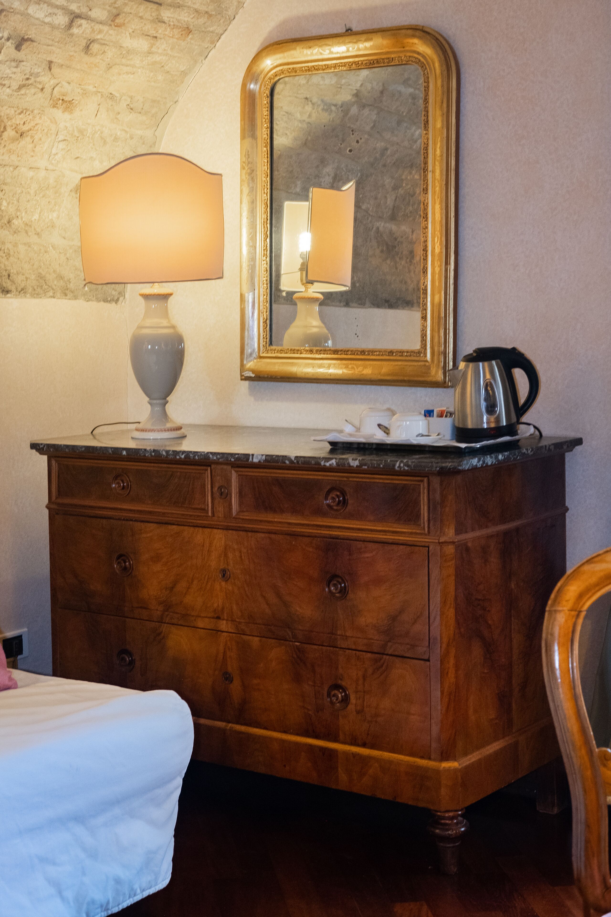 Une commode en bois, sur laquelle sont posés un miroir, une lampe et une bouilloire.