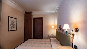 Una camera d'albergo con un letto, un comodino, una lampada, un quadro appeso alla parete e una porta.