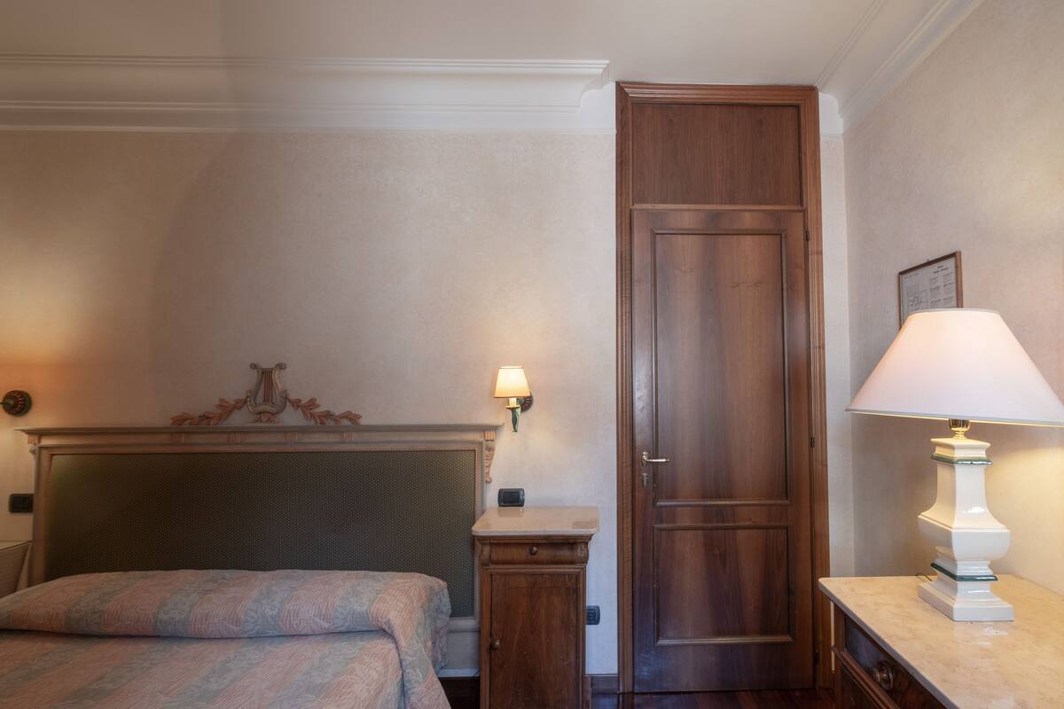 A hotel room with a bed, a nightstand, a lamp, and a wooden door.