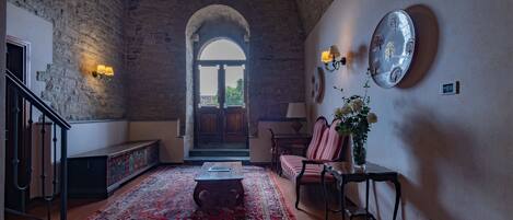 Amplia habitación con techo alto, un gran arco de entrada, un tapete rojo con diseño, una mesa de centro de madera, una silla a rayas rojas y blancas, una pequeña mesa con un jarrón de flores y un plato decorativo colgado en la pared.