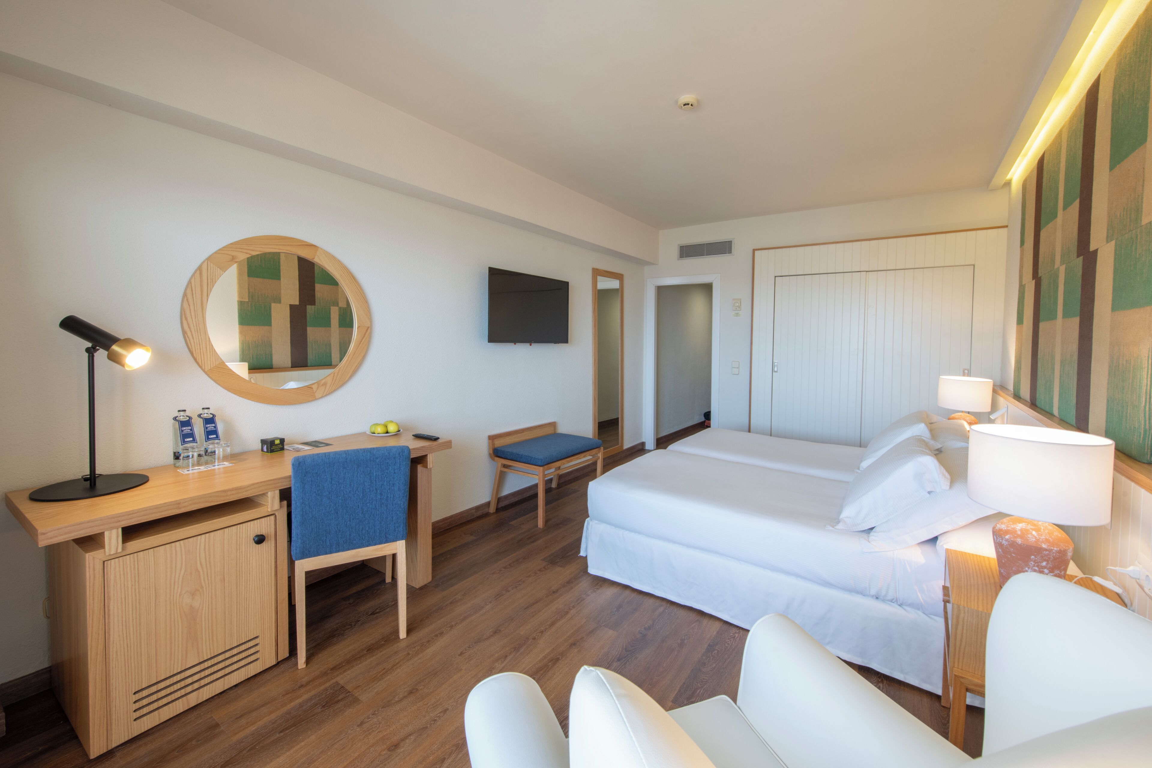 A hotel room with a bed, desk, chair, and a mirror.