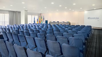 A conference room with rows of blue chairs, a podium, and flags.