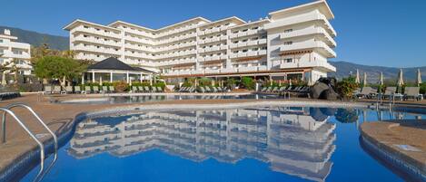 Ein Hotel mit großem Pool, mehreren Balkonen und Blick auf die Berge.