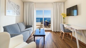 A modern living room with a sofa, a coffee table, a desk, and a TV. There is a large window with a view of the sea. - H10 Taburiente Playa (Brena Baja)