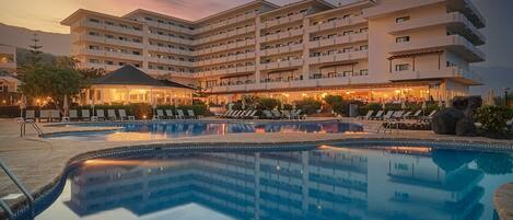 A hotel with a large swimming pool, multiple balconies, and a well-lit outdoor area.