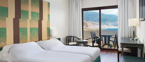 Habitación de hotel con dos camas, un escritorio, una silla y vistas a un paisaje montañoso.