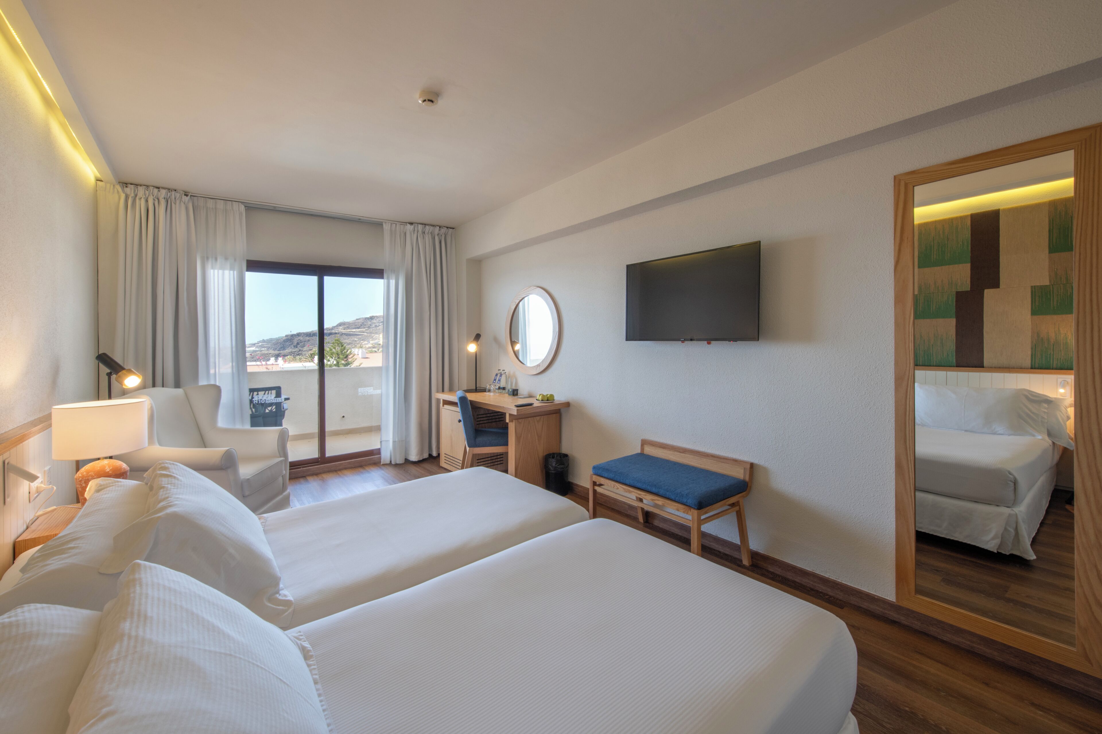 A hotel room with two beds, a desk, a chair, a TV, and a large mirror.