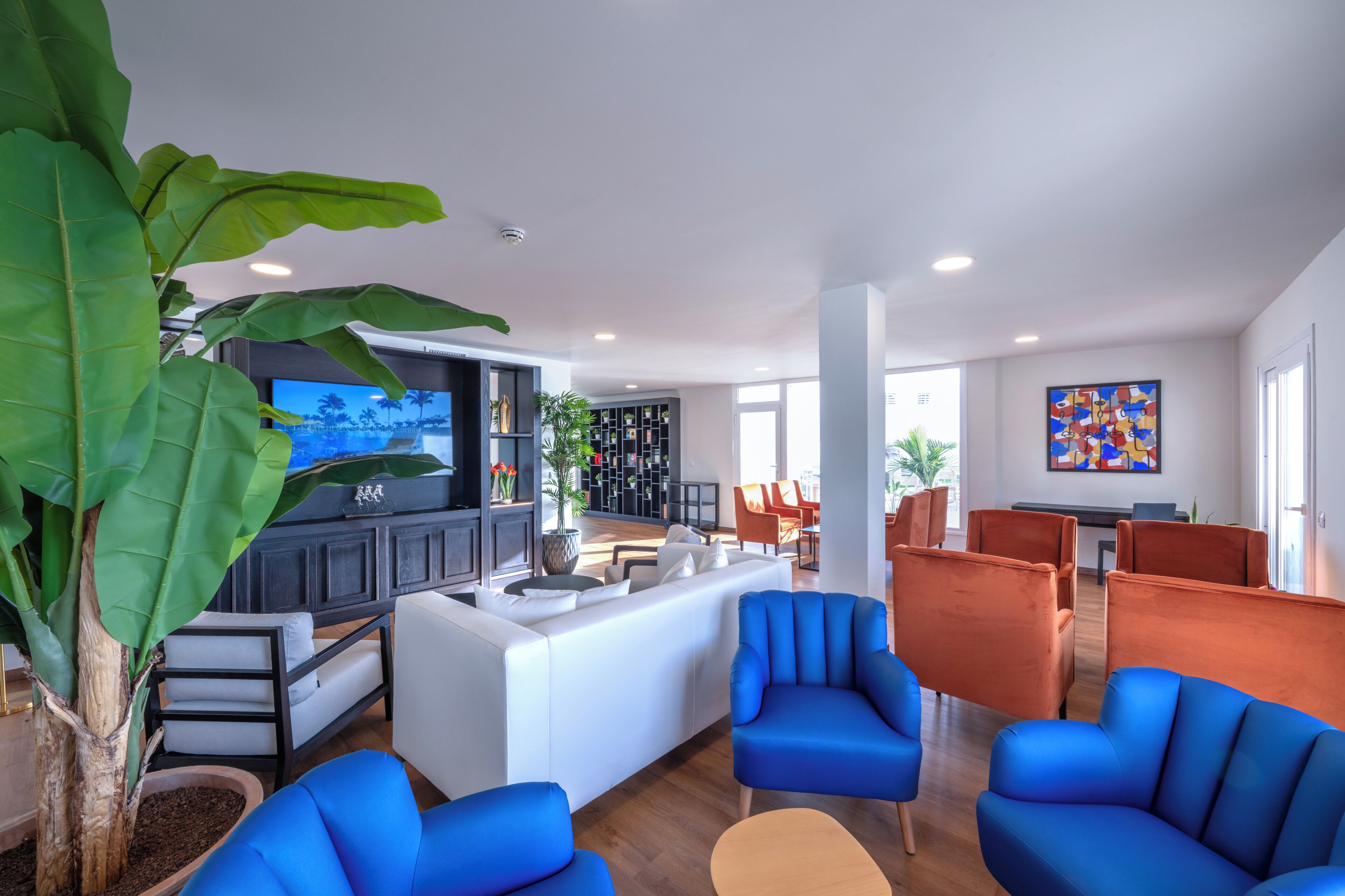 Un área de estar moderna con televisor, asientos y una planta.