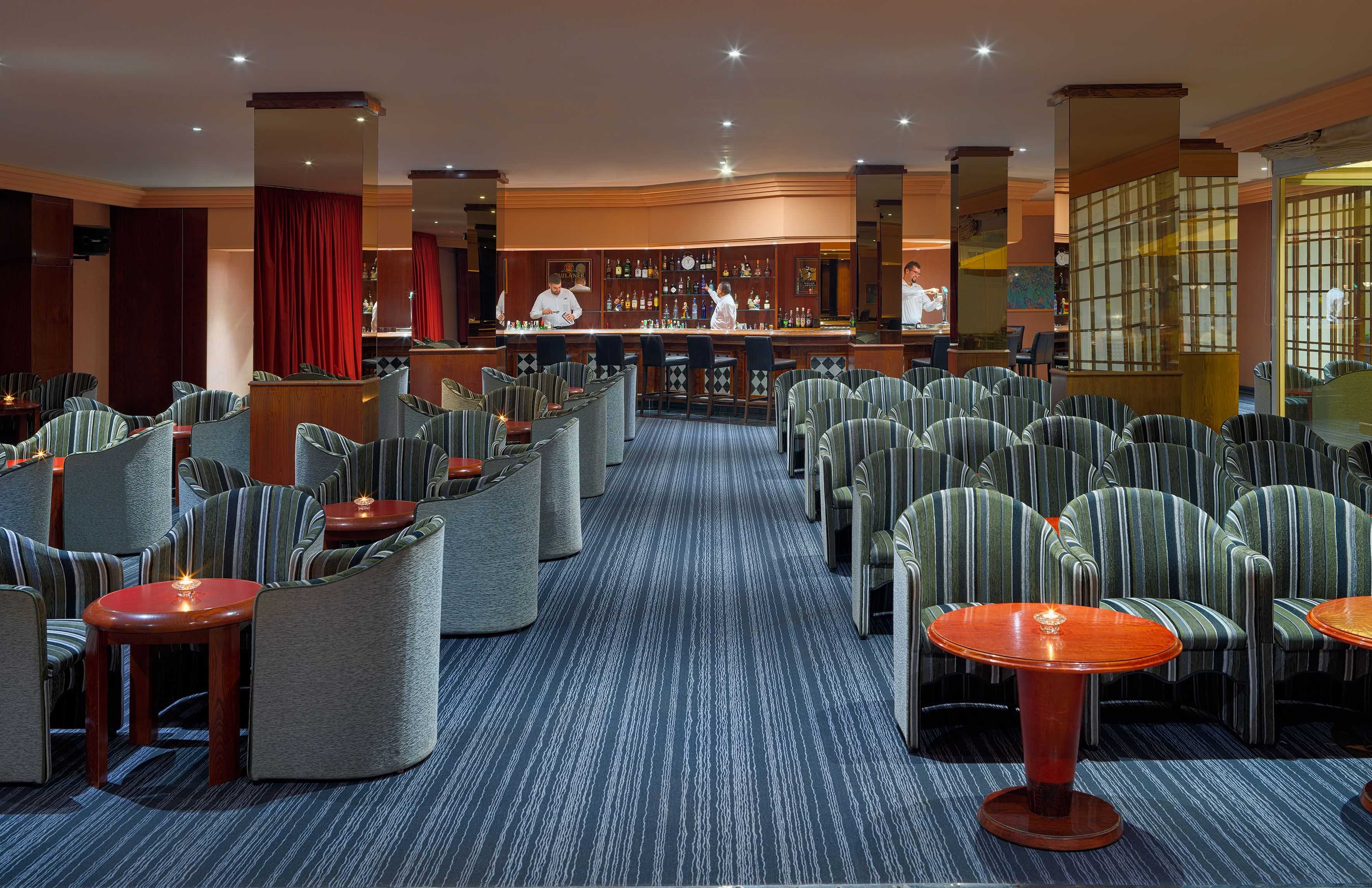 A hotel bar area with striped upholstered chairs, a bar counter, and a carpeted floor.
