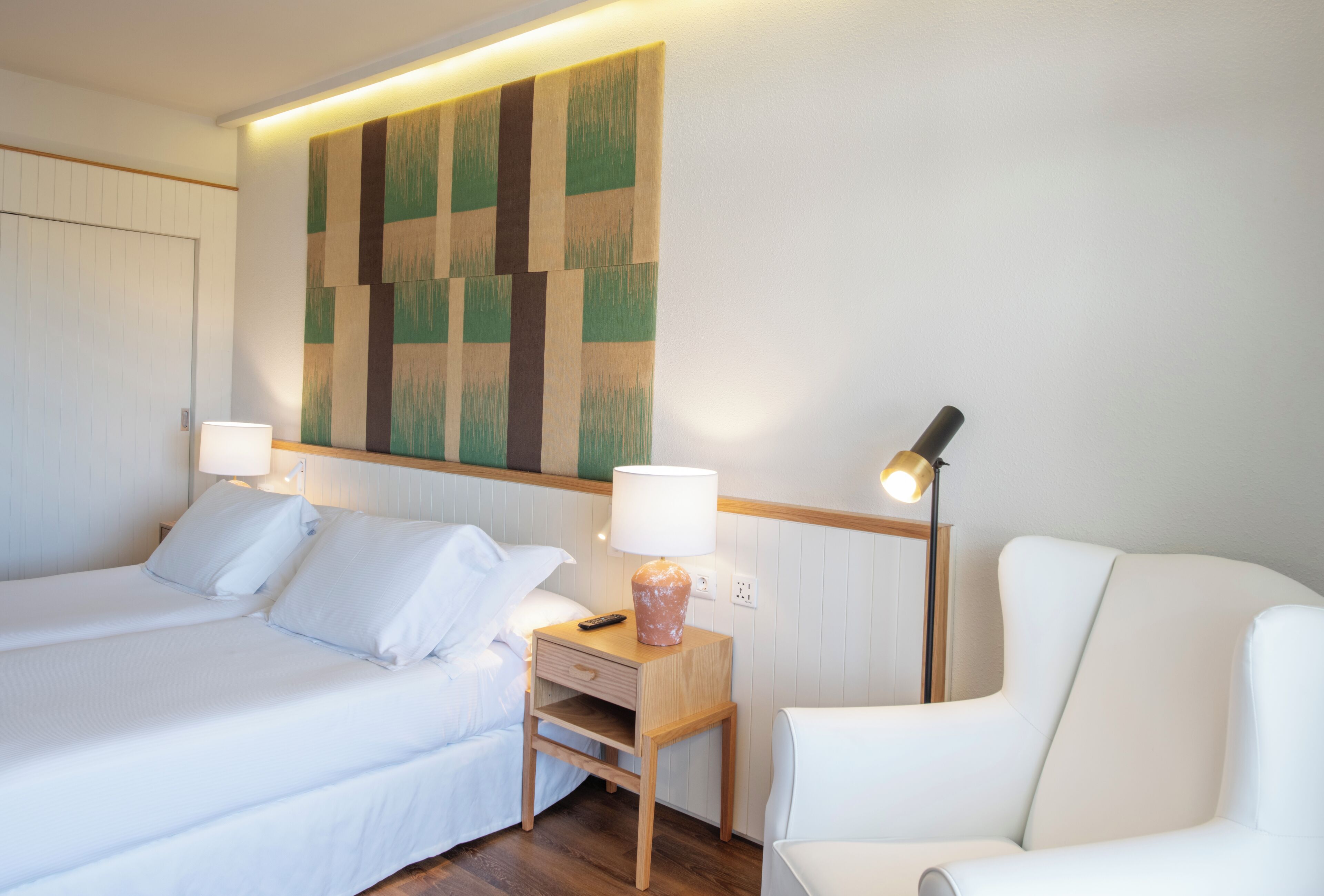 Een hotelkamer met twee bedden, een nachtkastje, een lamp, een stoel en een muur met een geometrisch patroon.